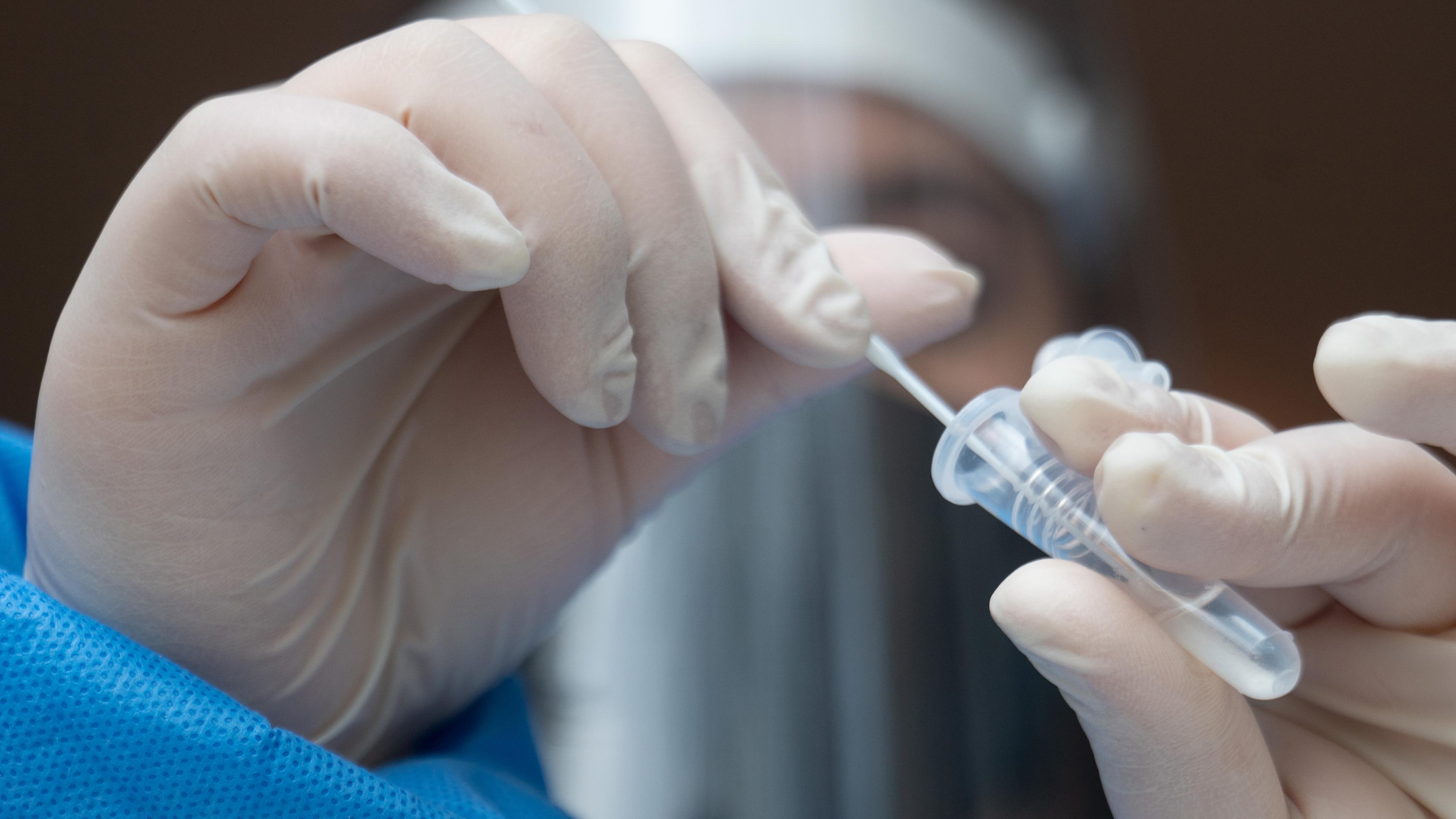 Ein Mitarbeiter einer Teststation hantiert mit einem Abstrichstäbchen für einen Schnelltest.