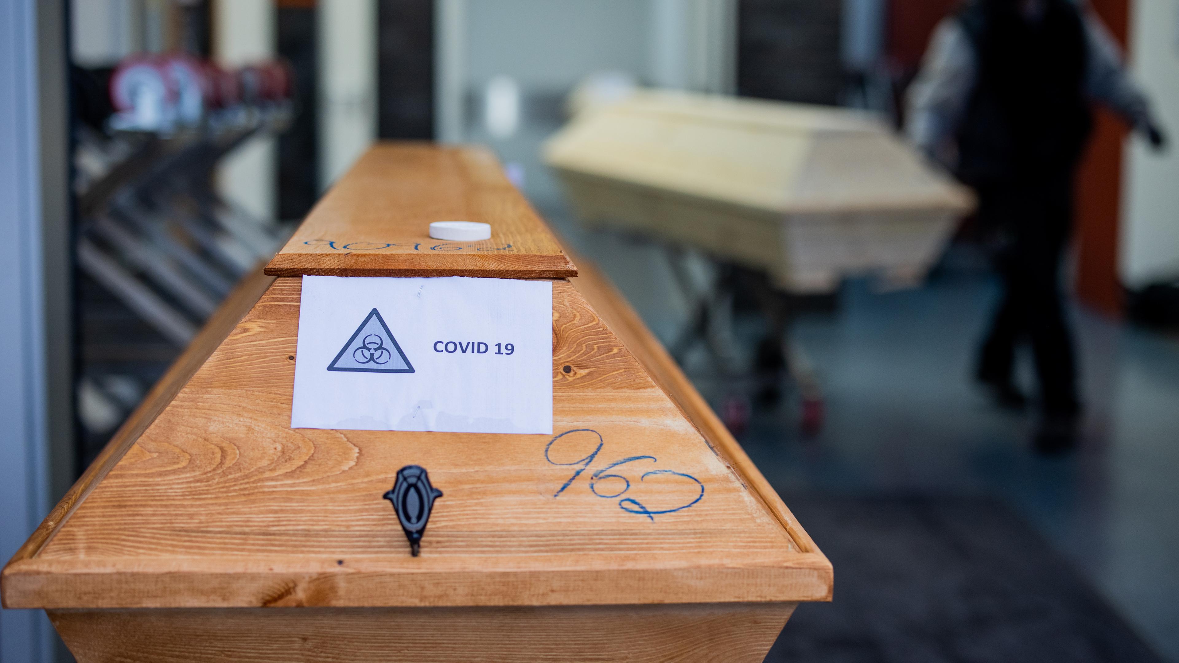 Nordrhein-Westfalen, Dülmen: Ein Sarg mit einem Verstorbenen mit der Aufschrift «Covid 19» und dem Zeichen «Biohazard» wird von einem Bestatter in ein Krematorium eingeliefert.