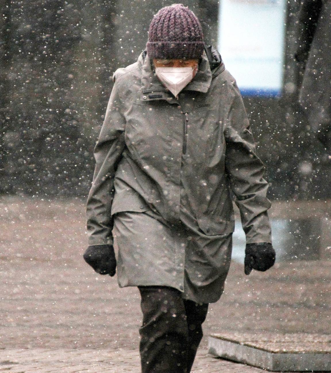 Eine Frau läuft mit FFP2-Maske durch Winterwetter mit Schnee