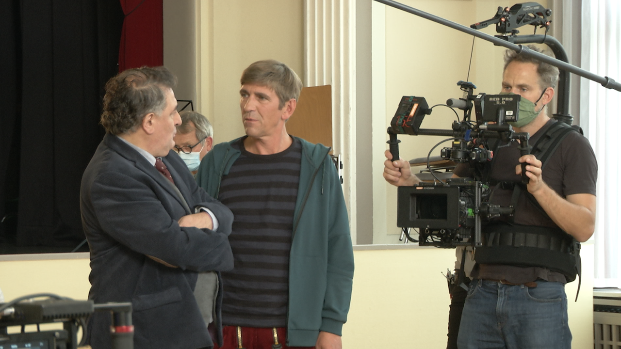Fritz Fuchs ist dem Musikschul-Direktor zugewant im Hintergund sieht man den Kamerman und die Crew.
