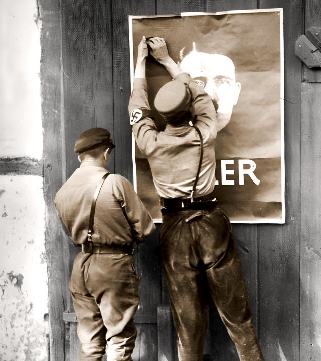 Junge Nationalsozialisten befestigen ein Wahlplakat für Hitler an einer Scheunentür