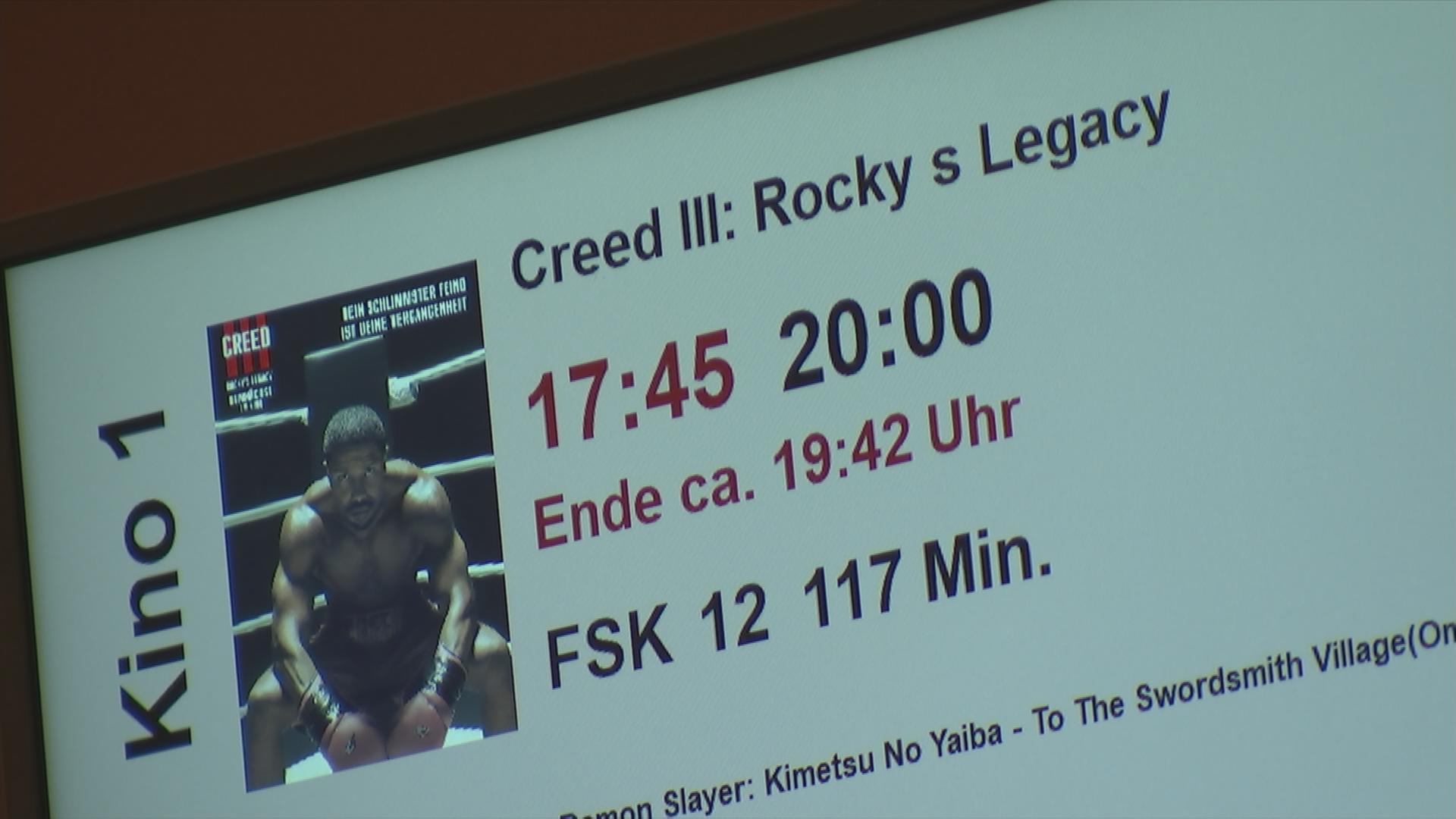 Auf dem Bild ist die Kinoanzeigetafel mit dem Film Creed 3 zu sehen.