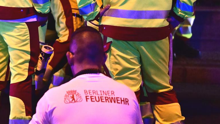 Eine in eine Rettungsdecke gehüllte Person steht neben Einsatzkräften der Feuerwehr nach dem Abbruch des Christopher Street Day (CSD)
