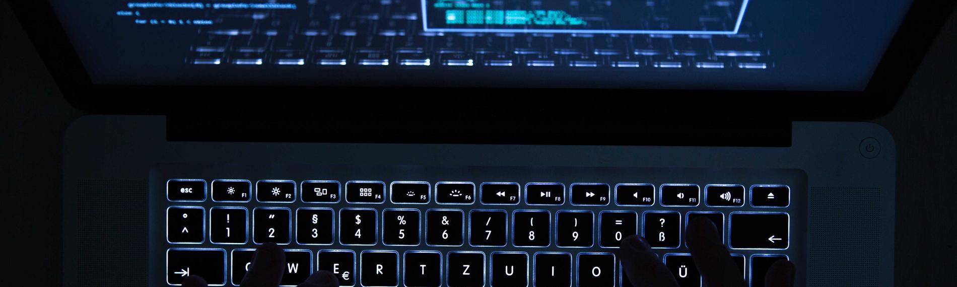 Ein mann bedient eine beleuchtete tastatur eines laptops. 