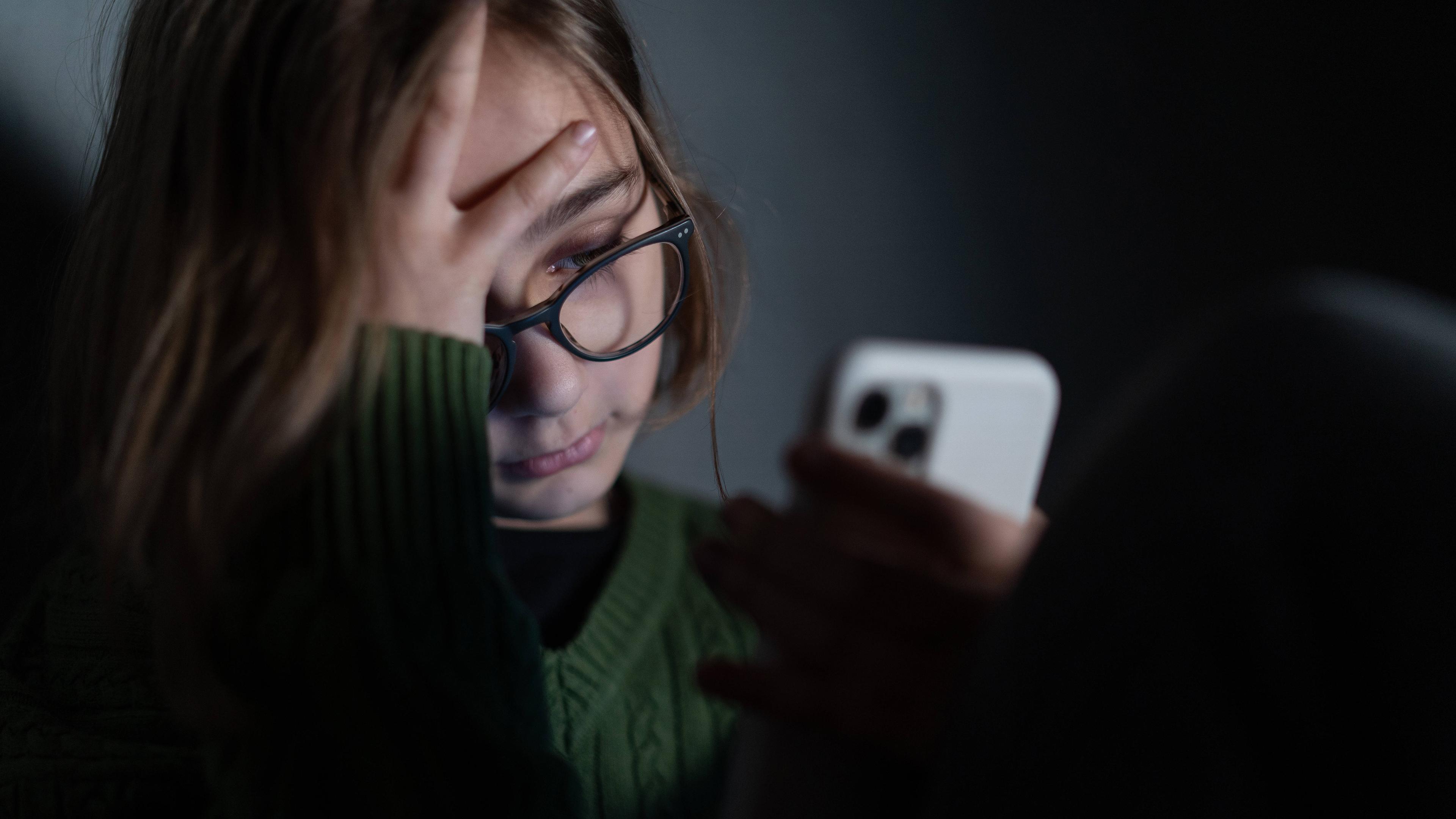 Ein trauriges Mädchen, sitzt allein in der Dunkelheit und benutzt ihr Smartphone (Symbolfoto)