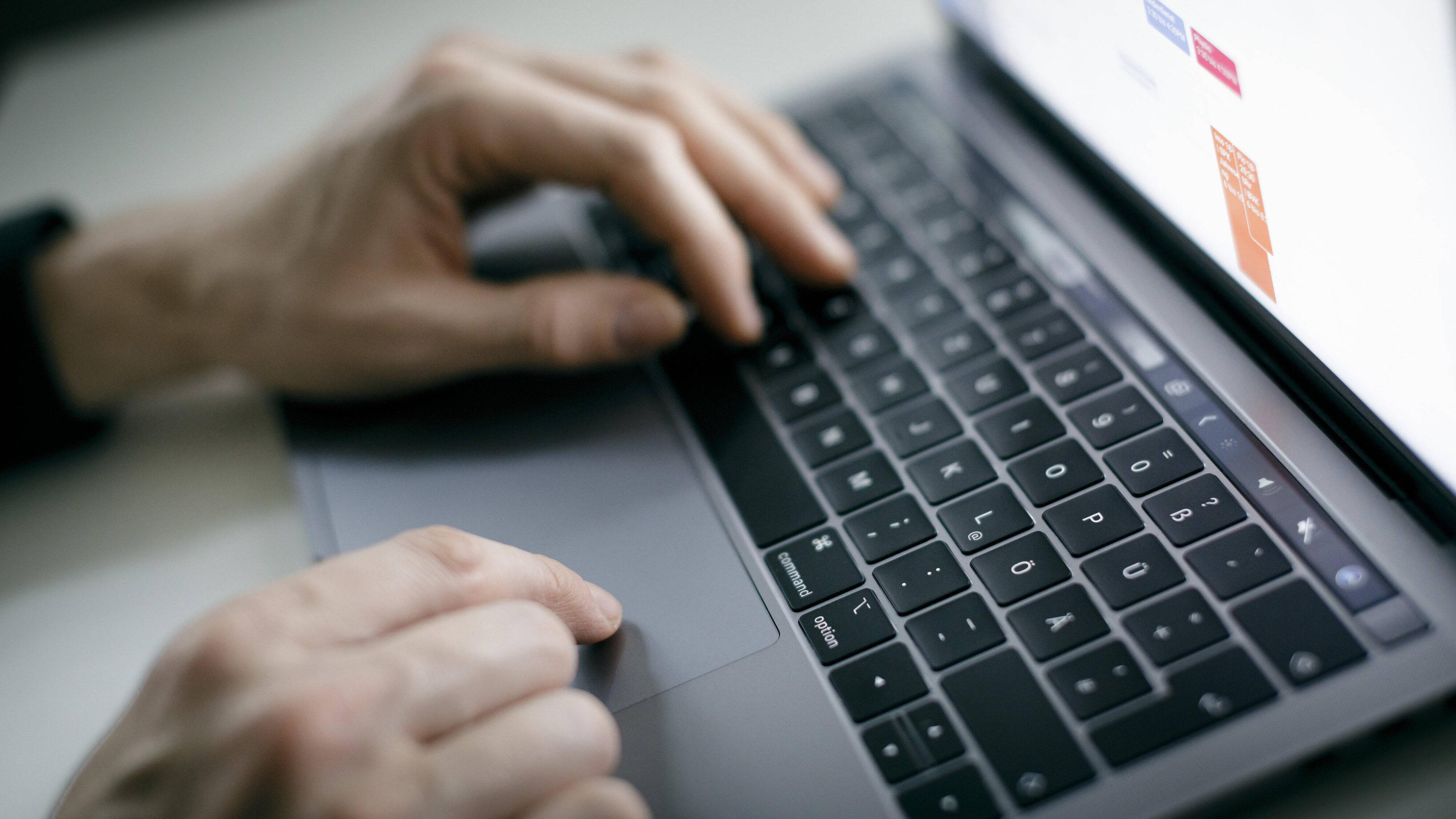 Hand eines Mannes auf der Tastatur eines Laptops
