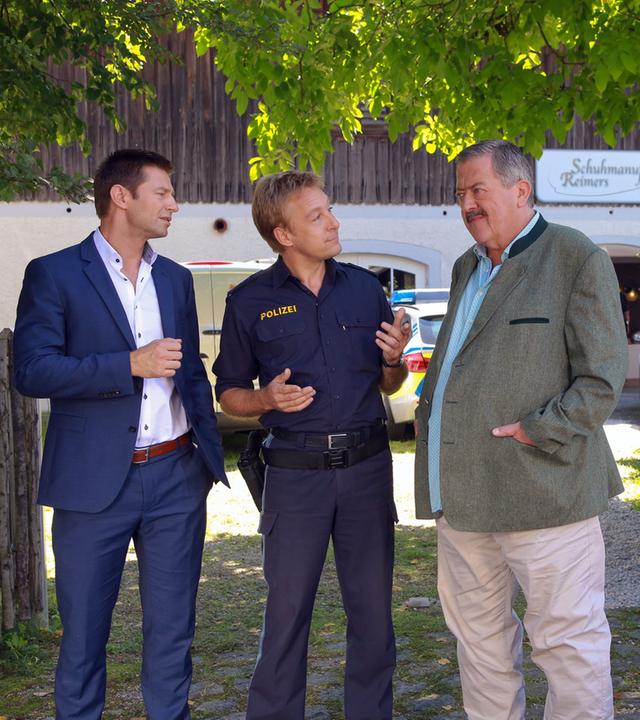 "Die Rosenheim-Cops - Da drückt der Schuh": Kommissar Hansen (Igor Jeftic), Polizist Mohr (Max Müller) und Kommissar Hofer (Joseph Hannesschläger) stehen in der Auffahrt zu einem Haus mit der Aufschrift "Schuhmanufaktur Reimers". Seitlich am Gartenzaun, an dem das gleiche Schild prangt, steht Maik Duschinsky (Markus Langer) mit verschränkten Armen. Er betrachtet die Ermittler.