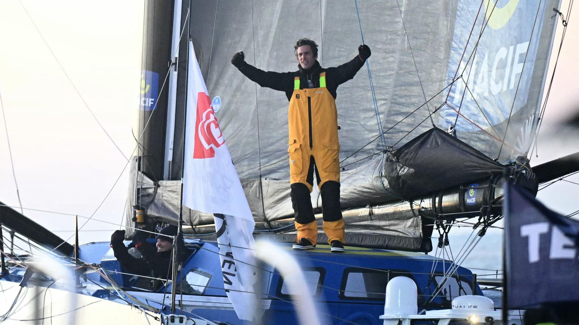 Vendee-Globe-Sieger Charlie Dalin im Ziel auf seinem Boot stehend.