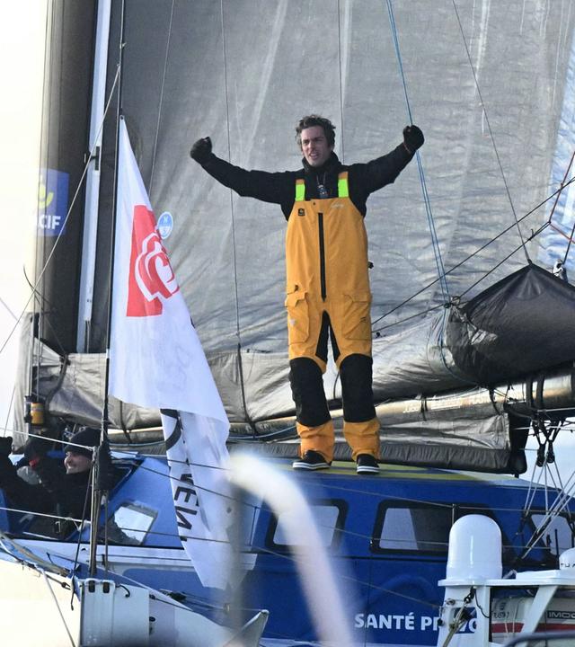 Vendee-Globe-Sieger Charlie Dalin im Ziel auf seinem Boot stehend.