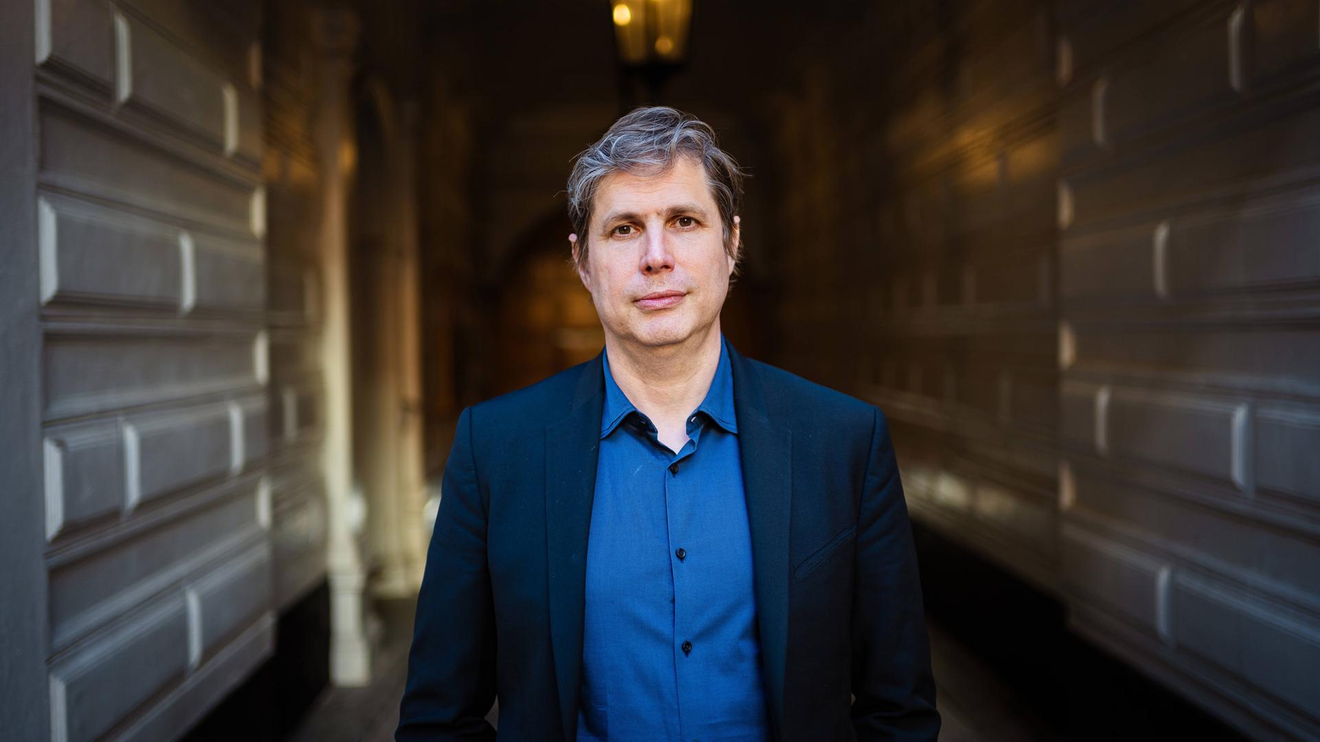 Porträtfoto eines Mannes mit leicht graumeliertem Haar in einer Toreinfahrt.