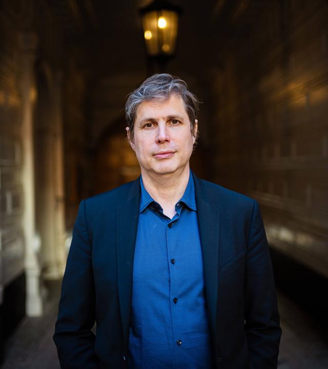 Porträtfoto eines Mannes mit leicht graumeliertem Haar in einer Toreinfahrt.