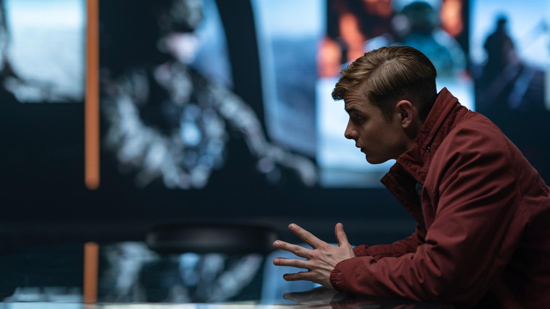 Alex Rider sitzend in einer roten Jacke