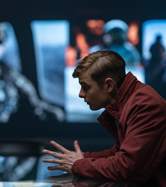 Alex Rider sitzend in einer roten Jacke