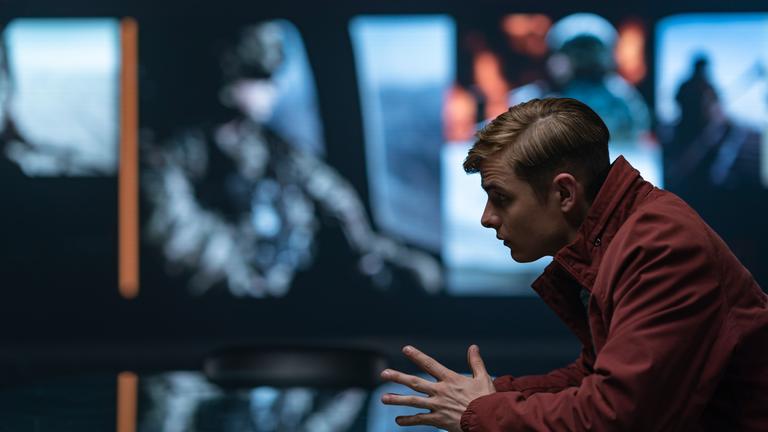 Alex Rider sitzend in einer roten Jacke