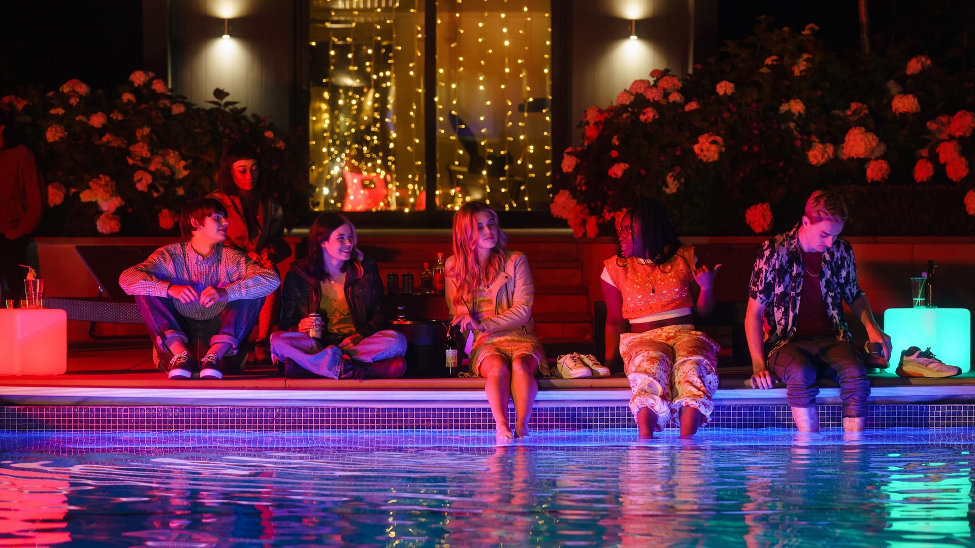 Tell me everything: Louis (Spike E. Fearn), Mei (Callina Liang), Regan (Tessa Lucille), Zia (Carla Woodcock), Neve (Lauryn Ajufo) und Jonny (Eden H. Davies) sitzen nachts an einem Pool, trinken Alkohol und unterhalten sich angeregt miteinander.