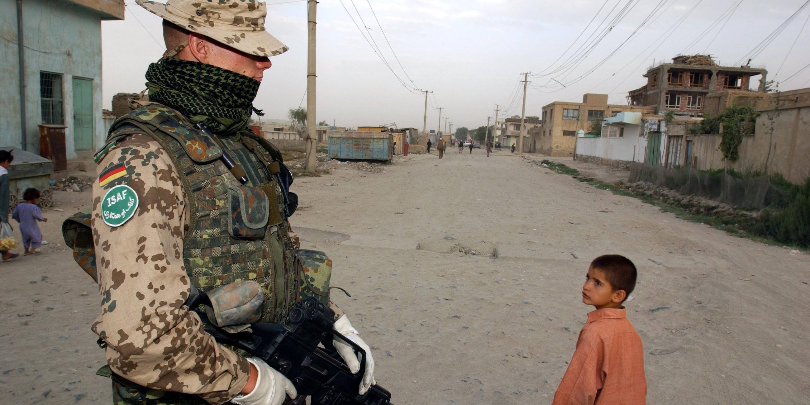  Ein Bundeswehrsoldat der Internationalen Afghanistan- Schutztruppe (ISAF) mit kugelsicherer Weste beobachtet am Montag, dem 04.08.2003 einen an ihm vorbei gehenden afghanischen Jungen in Karteparwan, einem nordoestlichen Stadtteil von Kabul.  