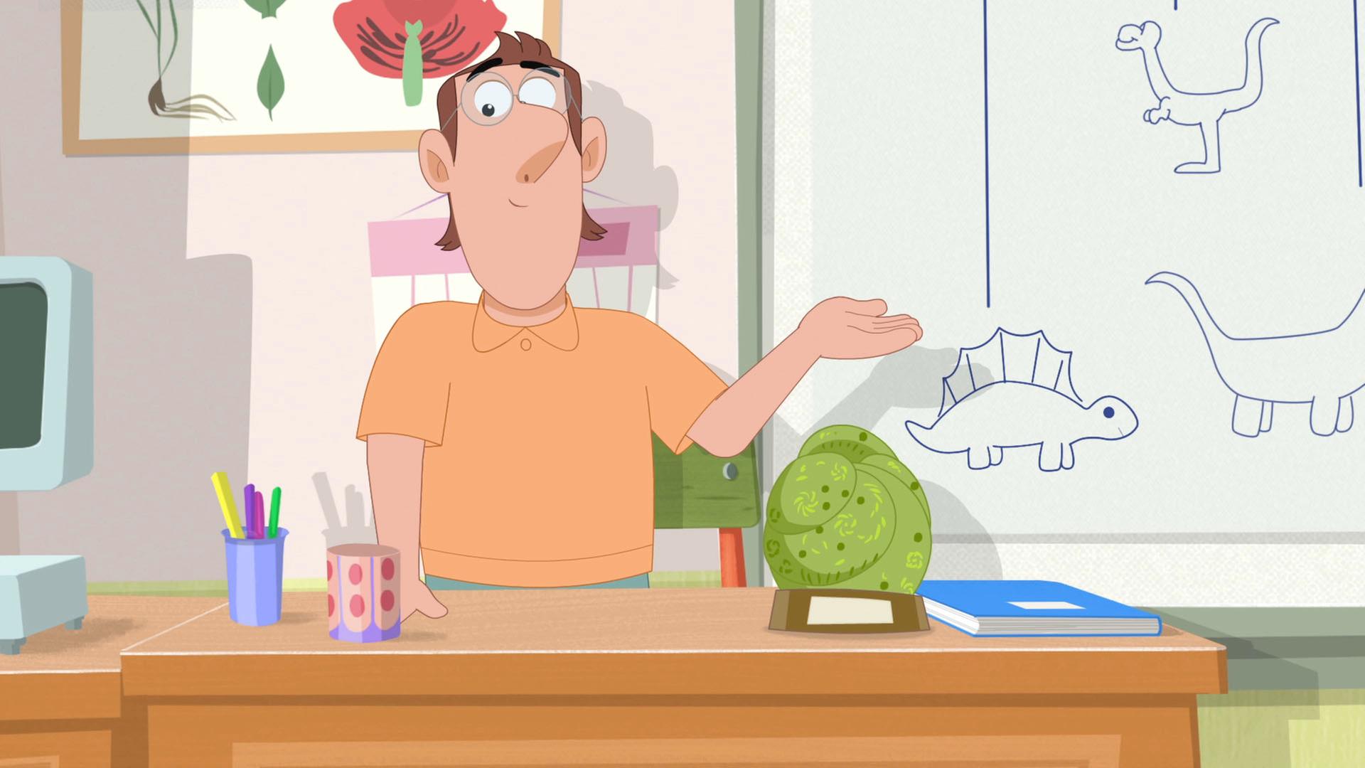 Herr Rebaud, Rebeccas Lehrer, steht hinter seinem Pult im Klassenzimmer und präsentiert das Dinosaurier-Fossil, welches auf dem Pult steht.