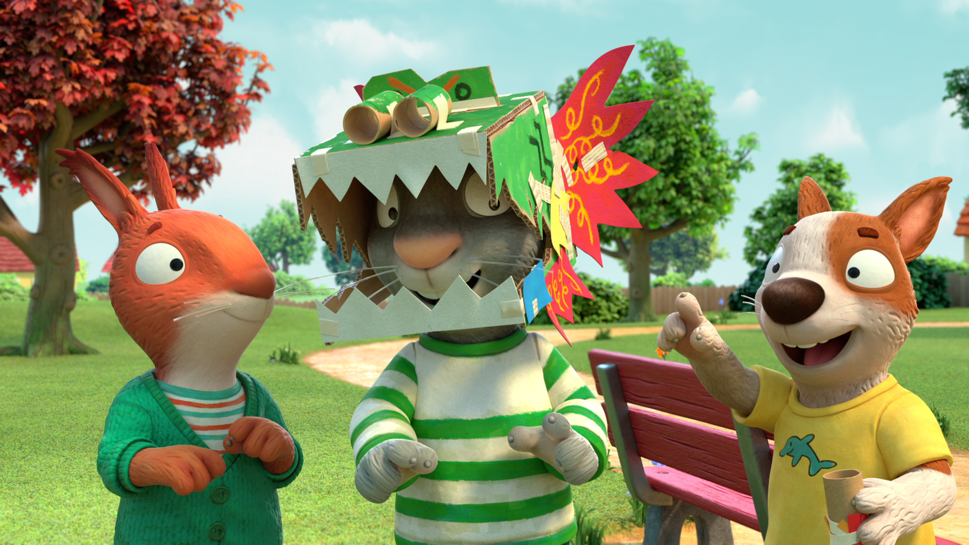 Pip steht zwischen Jamila (links) und Zac (rechts) und hat einen selbst gebastelten bunten Drachenkopf auf dem Kopf. Dieser ist aus Pappe und grün angestrichen udn hat hinten rote Drachenflügel.