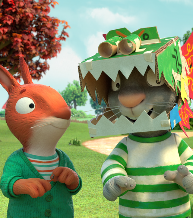 Pip steht zwischen Jamila und Zac und hat einen selbst gebastelten bunten Drachenkopf auf dem Kopf. Dieser ist aus Pappe und grün angestrichen und hat hinten rote Drachenflügel.