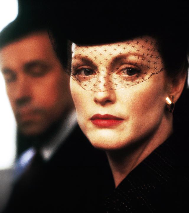Sarah (Julianne Moore) mit einem schwarzen Gesichtsschleier aus Spitze vor ihrem Gesicht. Henry (Stephen Rea) ist etwas verschwommen im Hintergrund zu sehen.