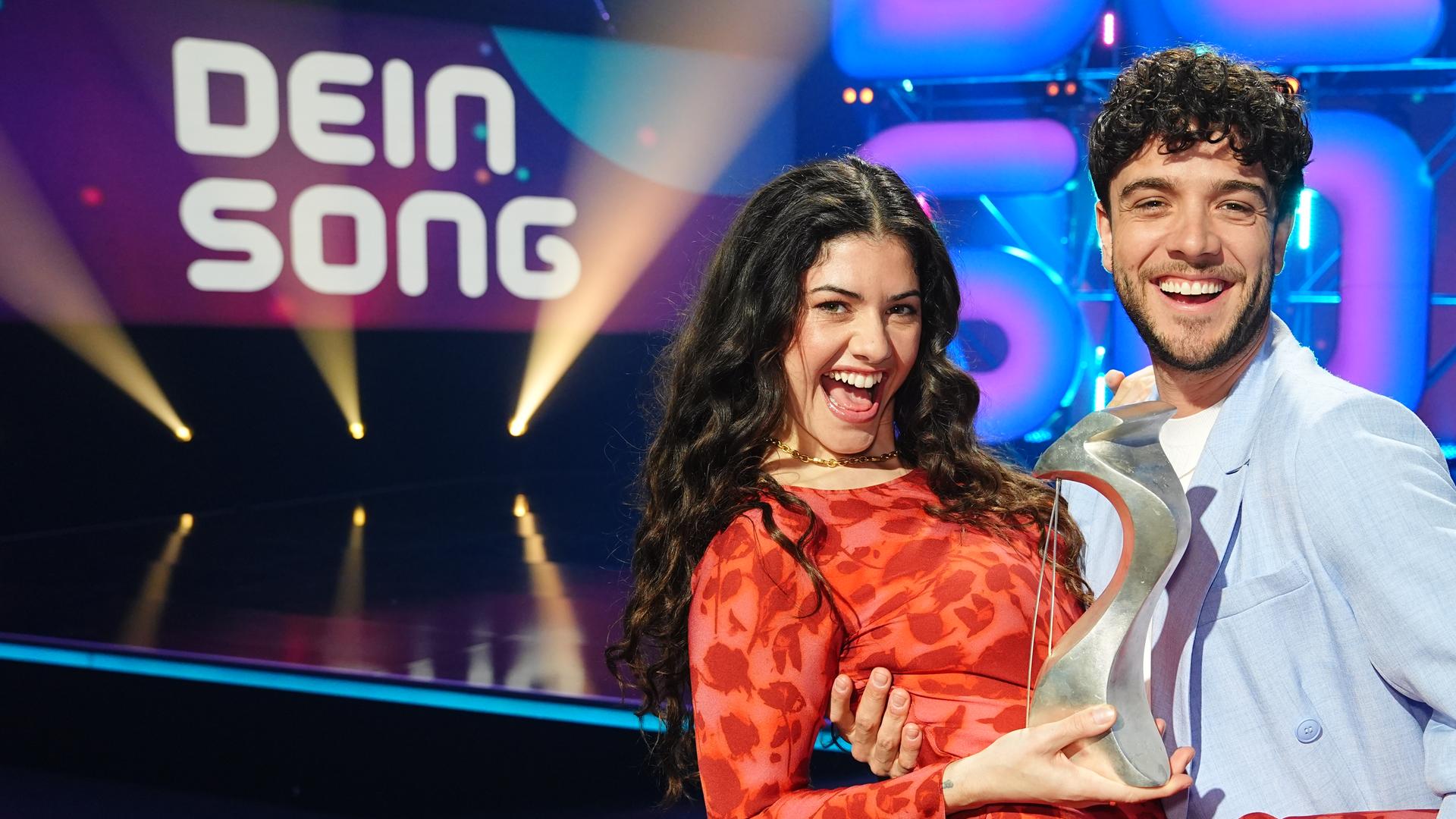 Jeannie Naomie Wagner und Luca Hänni stehen auf der "Dein Song" Bühne und halten den "Dein Song" Pokal in den Händen.