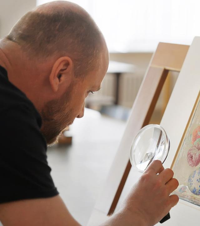 Ein Mann untersucht mit einer Lupe ein botanisches Aquarell mit Blumen von Maria Sibylla Merian.