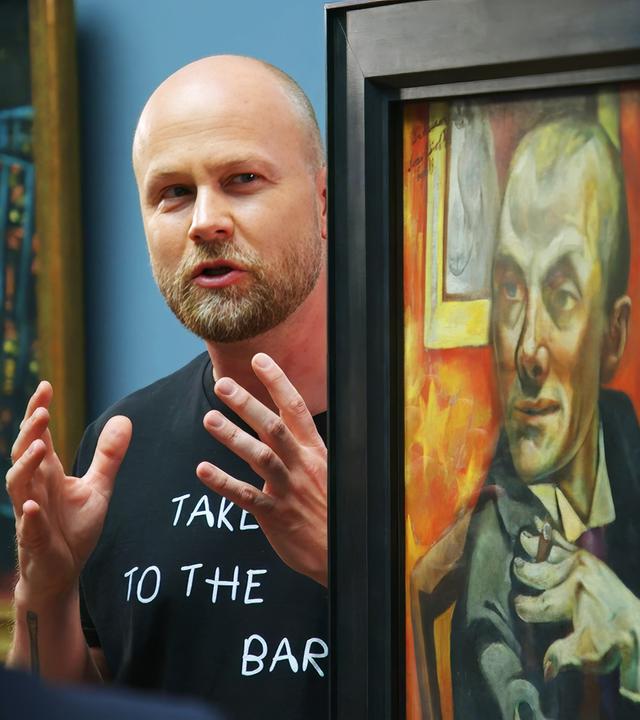 Ein Mann spricht vor einem Gemälde von Max Beckmann und gestikuliert mit den Händen.