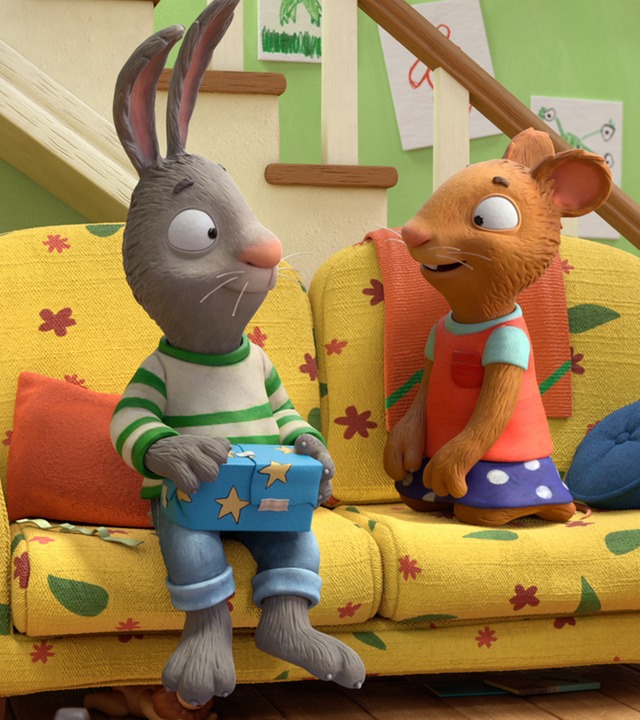 Pip und Posy sitzen auf dem Sofa. Pip hält freudestrahlend Posys Geschenk in der Hand.