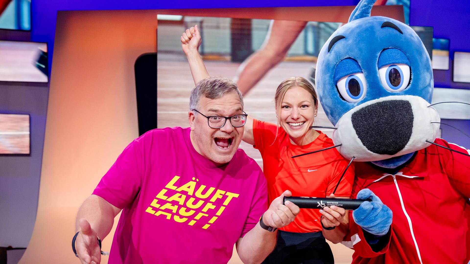 "1, 2 oder 3 - Das große Rennen": Elton, Sprinterin Lisa Mayer und Piet Flosse stehen im Studio vor dem "1, 2 oder 3"-Logo und strahlen in die Kamera.