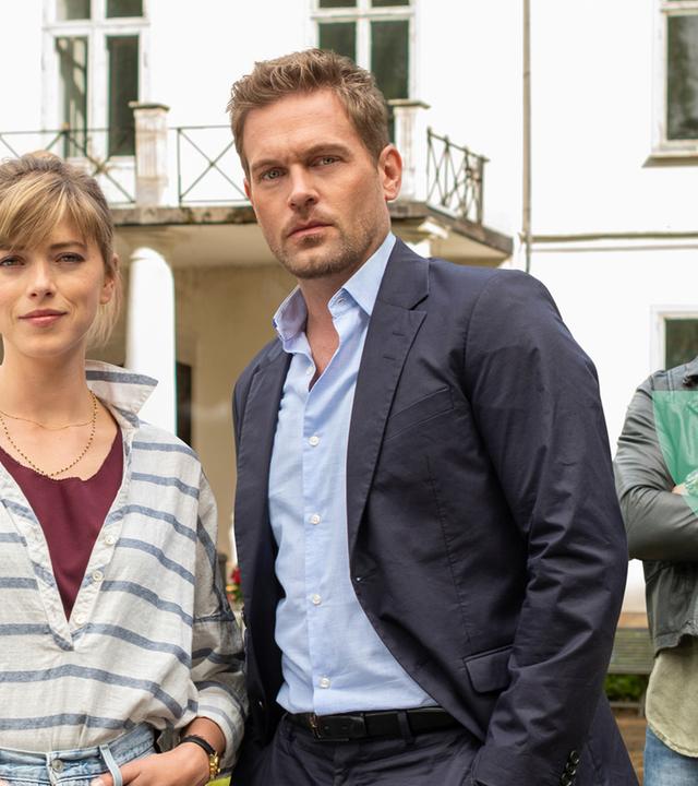 "Inga Lindström: Das Haus der 1000 Sterne": Stine (Mersiha Husagic), Paul (Joscha Kiefer) und Jan (Tony Kainz) stehen in der Einfahrt vor dem Haus und blicken in die Kamera.