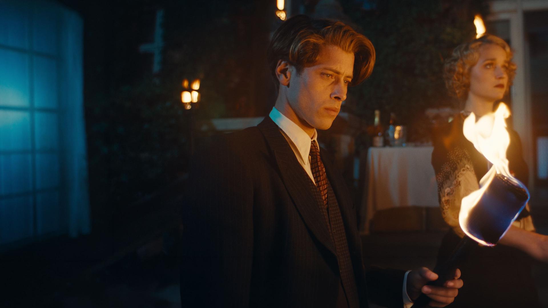 "This Is Not a Murder Mystery - Das Hummer-Telefon": René Magritte (Pierre Gervais) und Lee Miller (Florence Hall) stehen nebeneinander im Dunkeln. Im Vordergrund brennt eine Fackel, hinter den beiden sind weitere Lichter erkennbar.