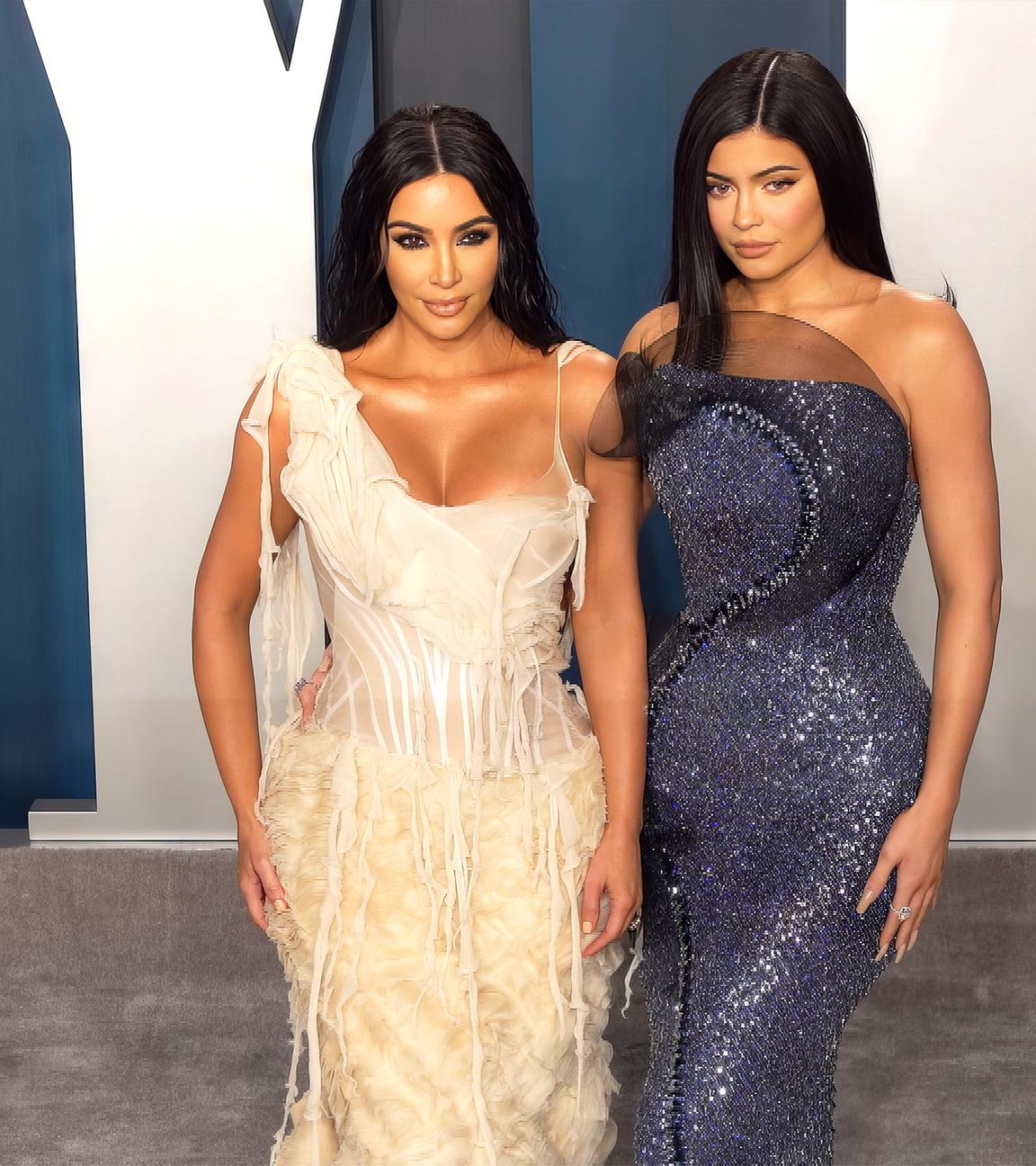 Kylie und Kim Kardashian stehen in Abendgarderobe auf einem grauen Teppich bei einer Veranstaltung.