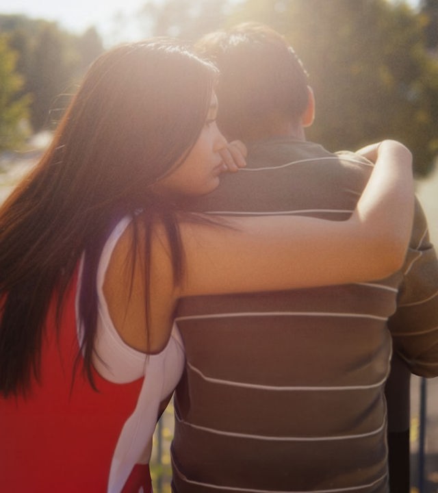 "After Benjamin: Das Konzert": Lina (Victoria Hoang) sitzt neben Elias (Sam Ashraf) im Freien mit dem Rücken zur Kamera auf einer Bank. Das Wetter ist schön, die Sonne scheint von vorn auf die beiden. Lina sitzt Elias zugewandt, umarmt ihn mit ihrem rechten Arm und lehnt ihr Kinn auf seine Schulter. Elias schaut geradeaus, den Kopf leicht nach unten gebeugt.