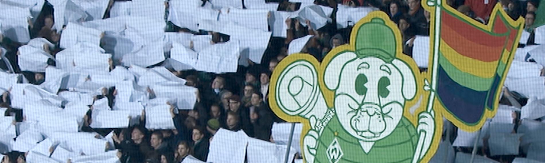 Blick von schräg oben: Fans im Stadion halten weiße Plakate als Zeichen gegen Homophobie.