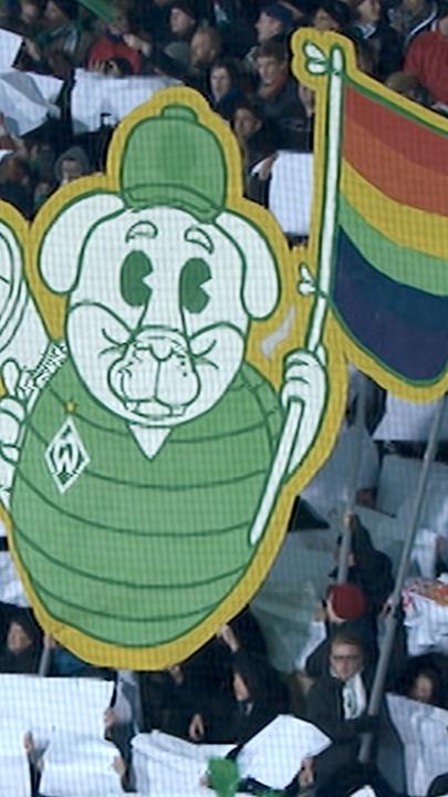 Blick von schräg oben: Fans im Stadion halten weiße Plakate als Zeichen gegen Homophobie.