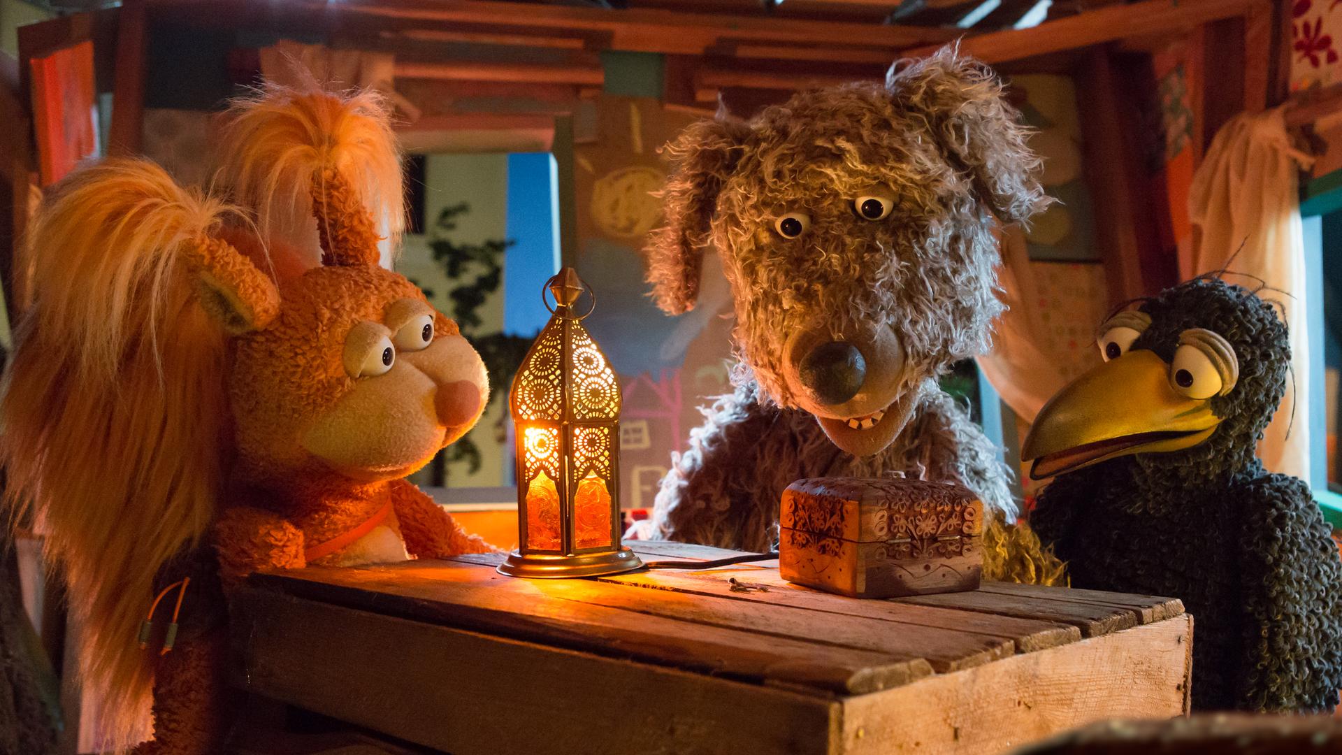 Ella, Buffo und Rudi sitzen im Baumhaus und schauen auf ein verschlossenes Kästchen das vor ihnen auf dem Tisch liegt.