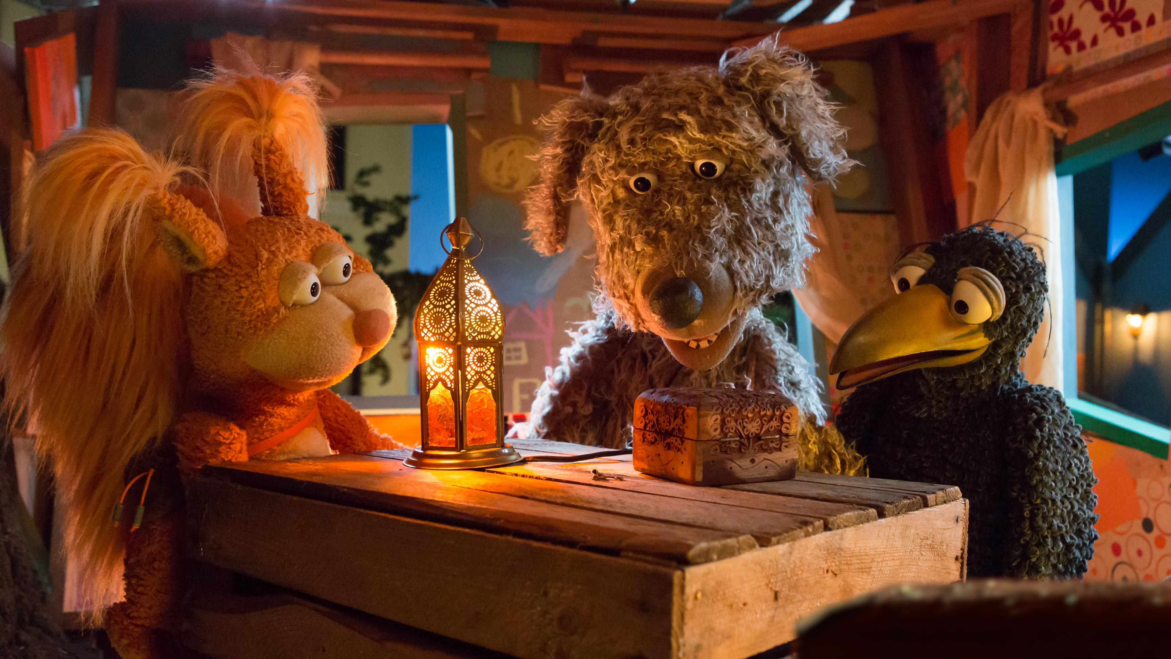 Ella, Buffo und Rudi sitzen im Baumhaus und schauen auf ein verschlossenes Kästchen das vor ihnen auf dem Tisch liegt.
