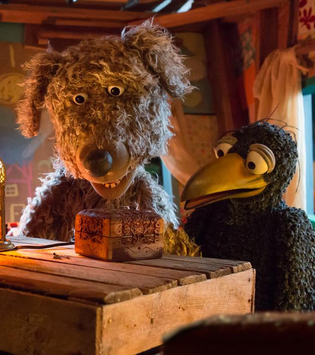 Ella, Buffo und Rudi sitzen im Baumhaus und schauen auf ein verschlossenes Kästchen das vor ihnen auf dem Tisch liegt.