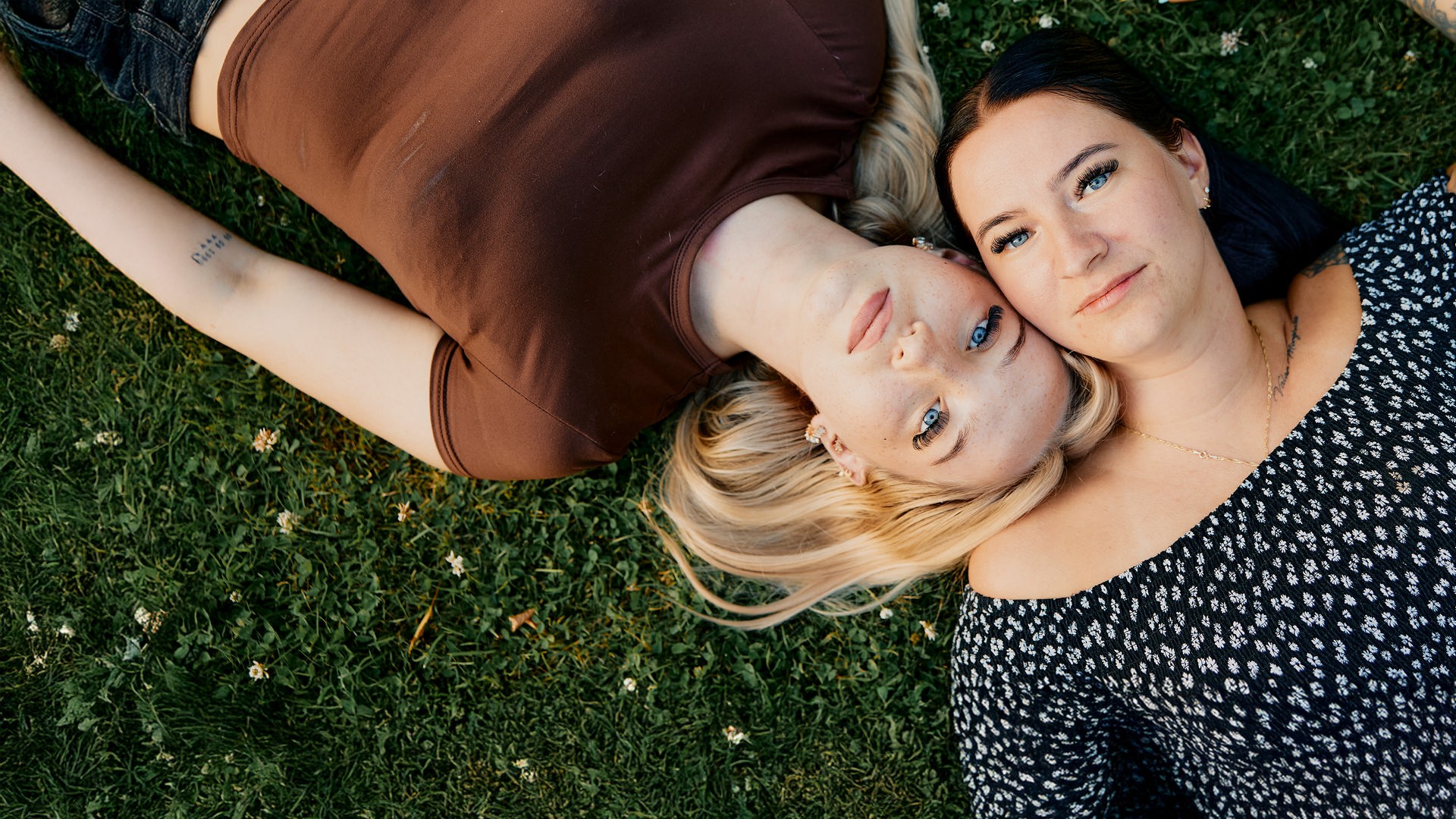 Blick von oben: Jaqueline und Caithlen liegen auf dem Rasen und berühren sich an der Hand.