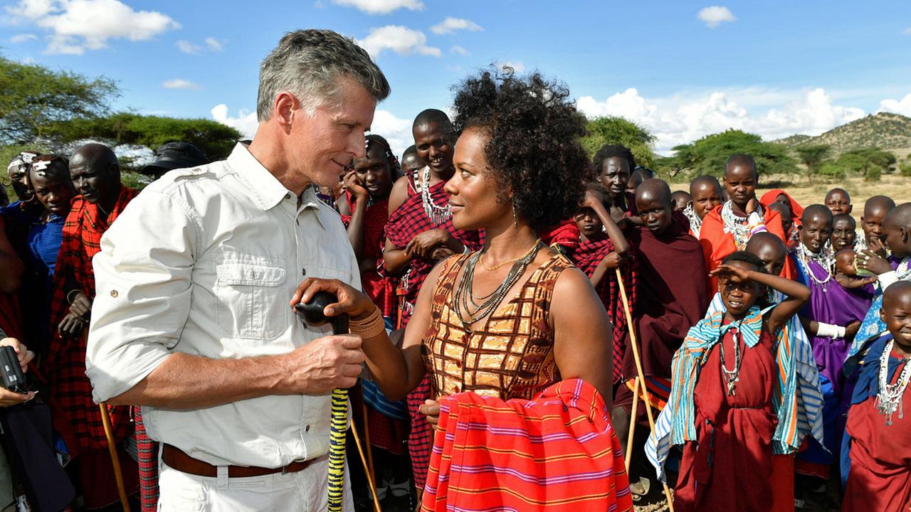 "Das Traumschiff: Tansania": Dr. Sander (Nick Wilder) steht Loveness (Denise M'Baye) gegenüber. Beide blicken sich tief in die Augen. Im Hintergrund stehen Einheimische und beobachten die beiden.