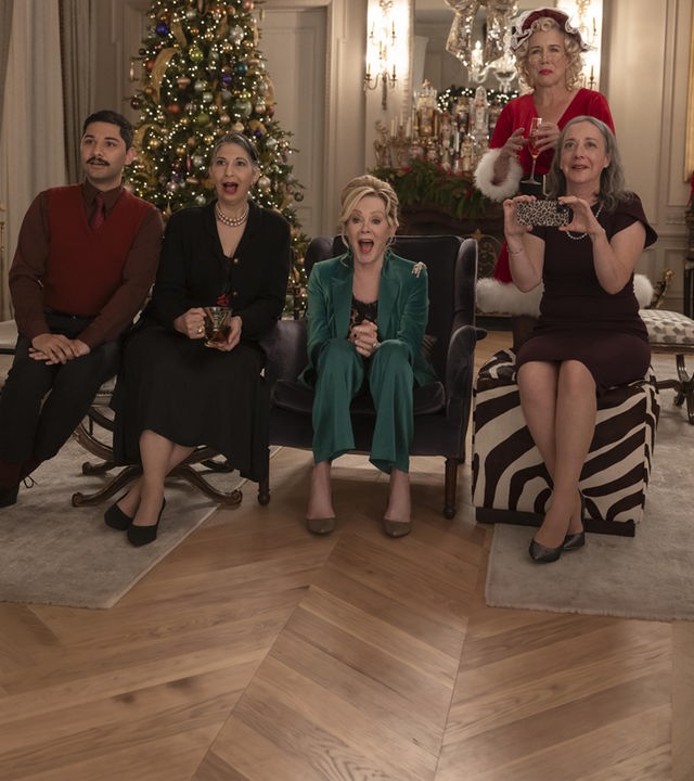 "Hacks - Das Vegas-Weihnachtsspektakel": In festlicher Kleidung sitzen Damien (Mark Indelicato), Josefina (Rose Abdoo), Deborah (Jean Smart) und Avas Mutter Nina (Jane Adams) lachend nebeneinander in einem festlich geschmückten Wohnraum. Hinter ihnen steht Bürgermeisterin Mayor Jo (Lauren Weedman) im Santa-Kostüm. An der Seite steht ein großer Weihnachtsbaum.