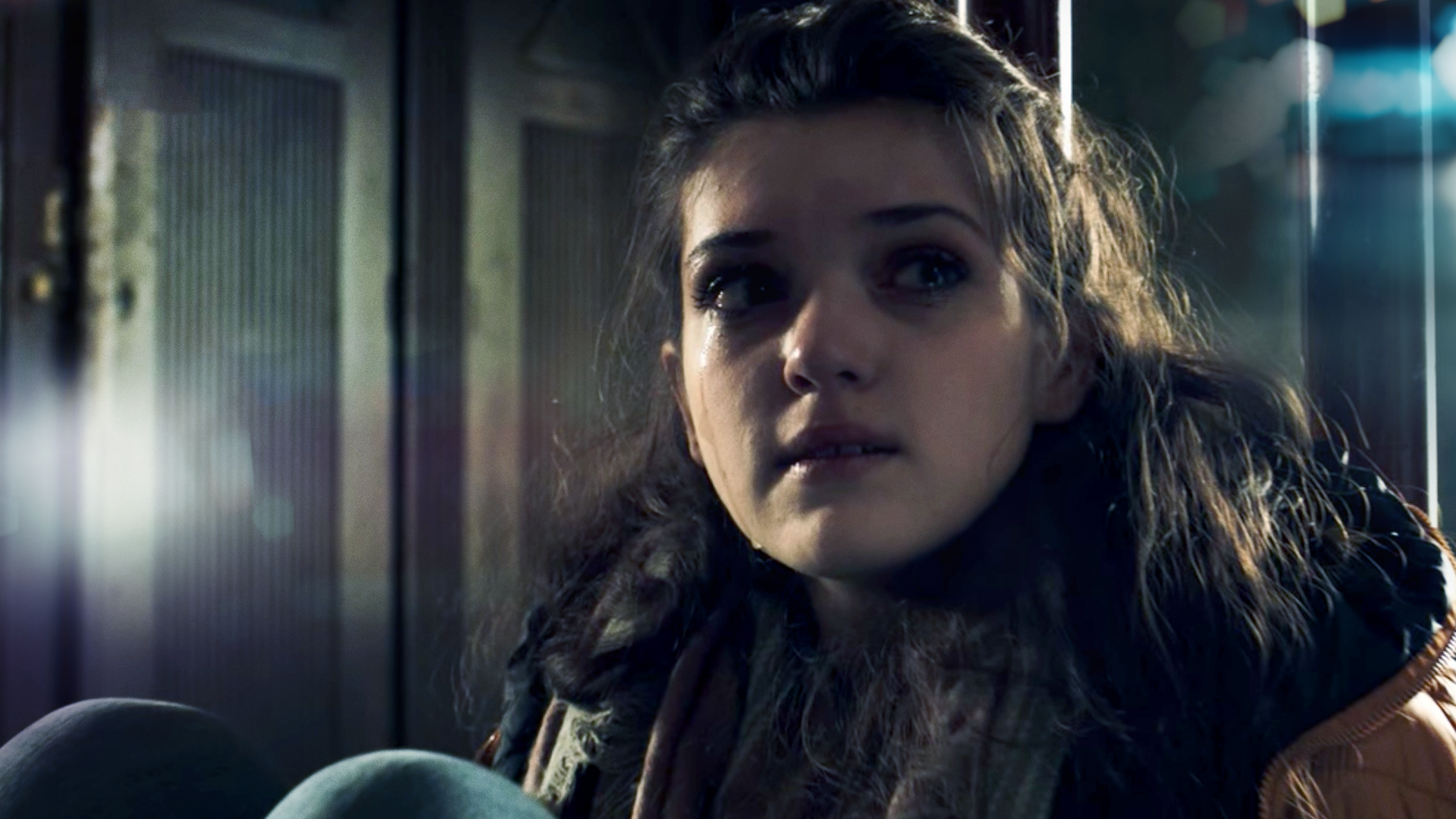 Ein Mädchen sitzt zusammemgekauert in einem dunklen Raum und blickt in Richtung des Lichts.