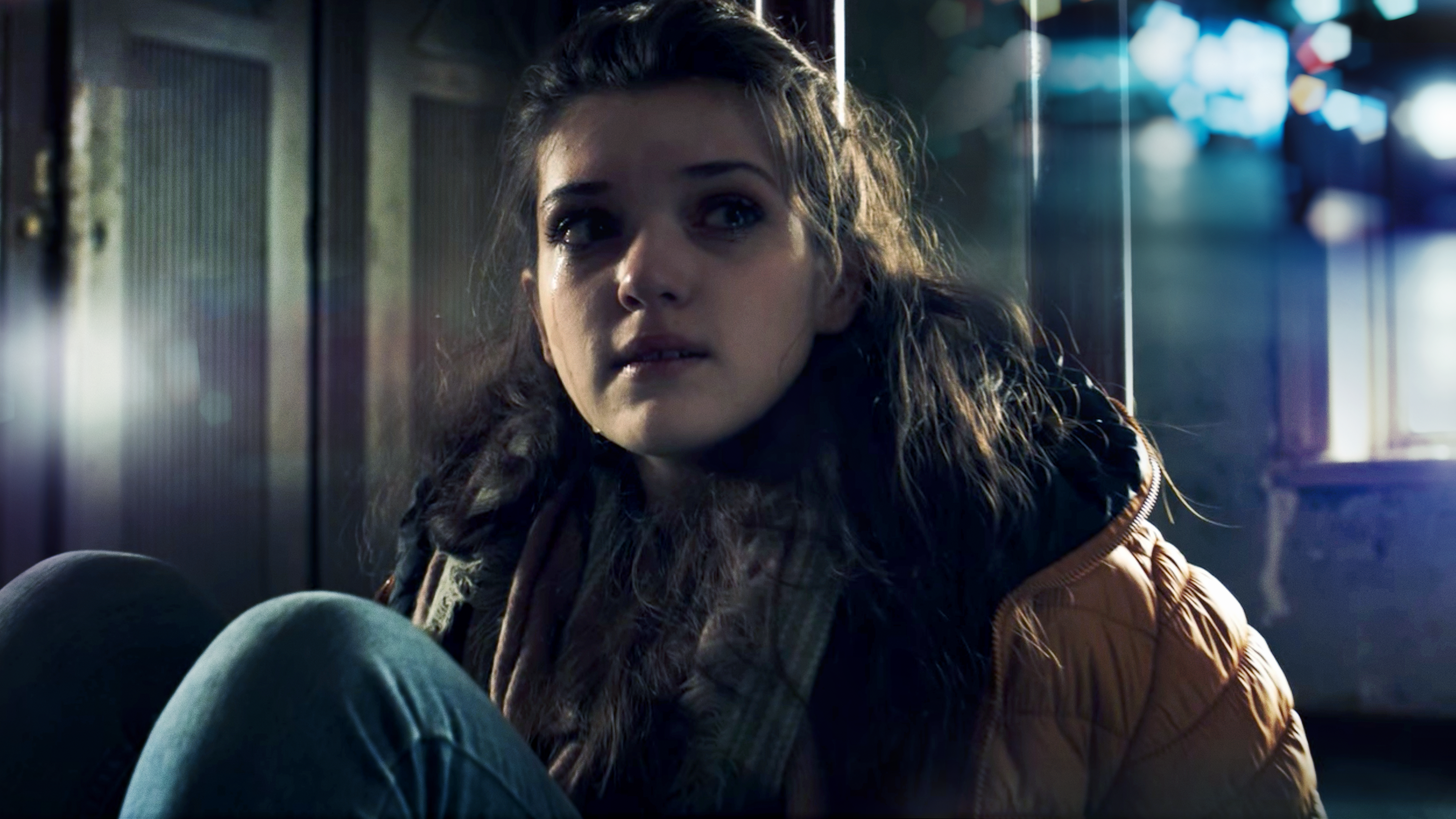 Ein Mädchen sitzt zusammemgekauert in einem dunklen Raum und blickt in Richtung des Lichts.