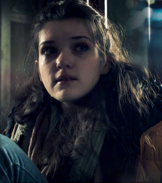 Ein Mädchen sitzt zusammemgekauert in einem dunklen Raum und blickt in Richtung des Lichts.