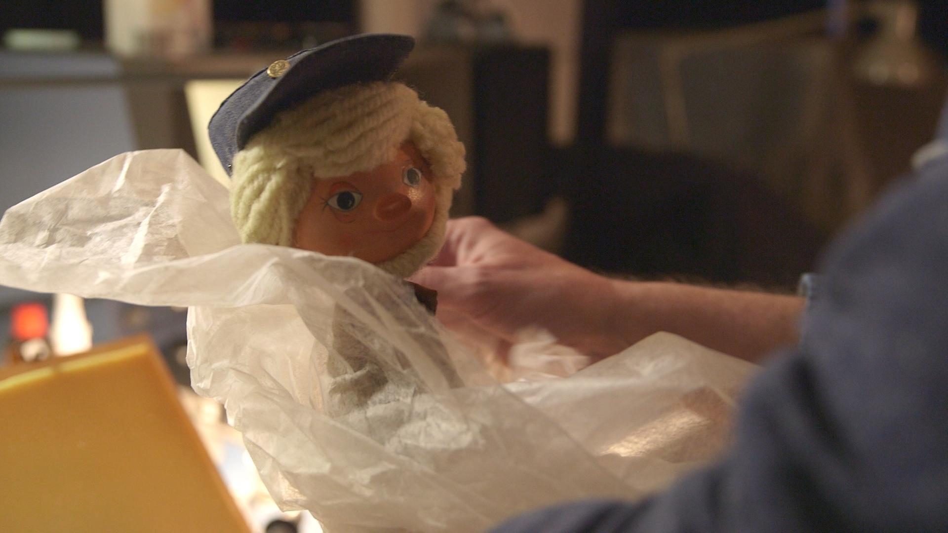 "Das war dann mal weg: Ostmark, Westsandmann & Transitstrecke": Jemand hält die Puppe des Westsandmännchens in die Kamera.