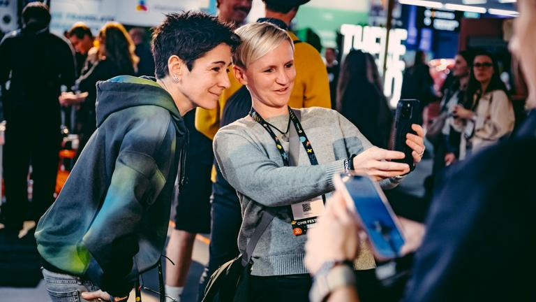 ZDF-Moderatorin macht mit einer Besucherin auf der Messe OMR 2025 in Hamburg ein gemeinsames Selfi. Im Hintergrund Messebetrieb.