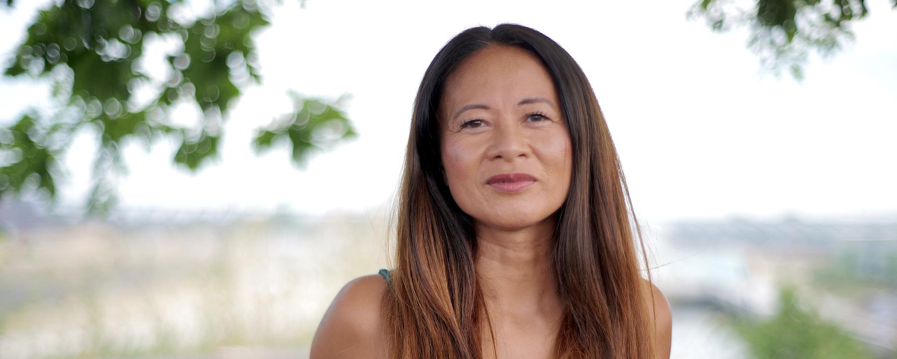 Portrait einer asiatischen Frau mit braunen langen Haaren. Sie lächelt in die Kamera.