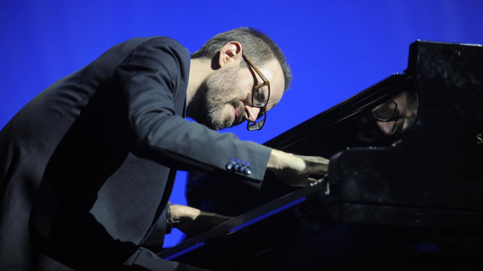 Ein Mann mit Brille und Bart beugt sich über ein Klavier und spielt.