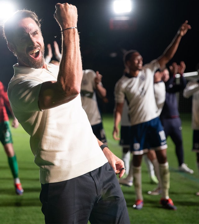 "Dear England (4)": Bei Flutlicht nachts im Stadion auf dem Rasen: Im Vordergrund reckt Gareth Southgate (Joseph Fiennes) seinen rechten Arm mit geballter Faust vor Kraft strotzend in die Höhe. Hinter ihm befindet sich seine Mannschaft, die ebenfalls jubiliert.