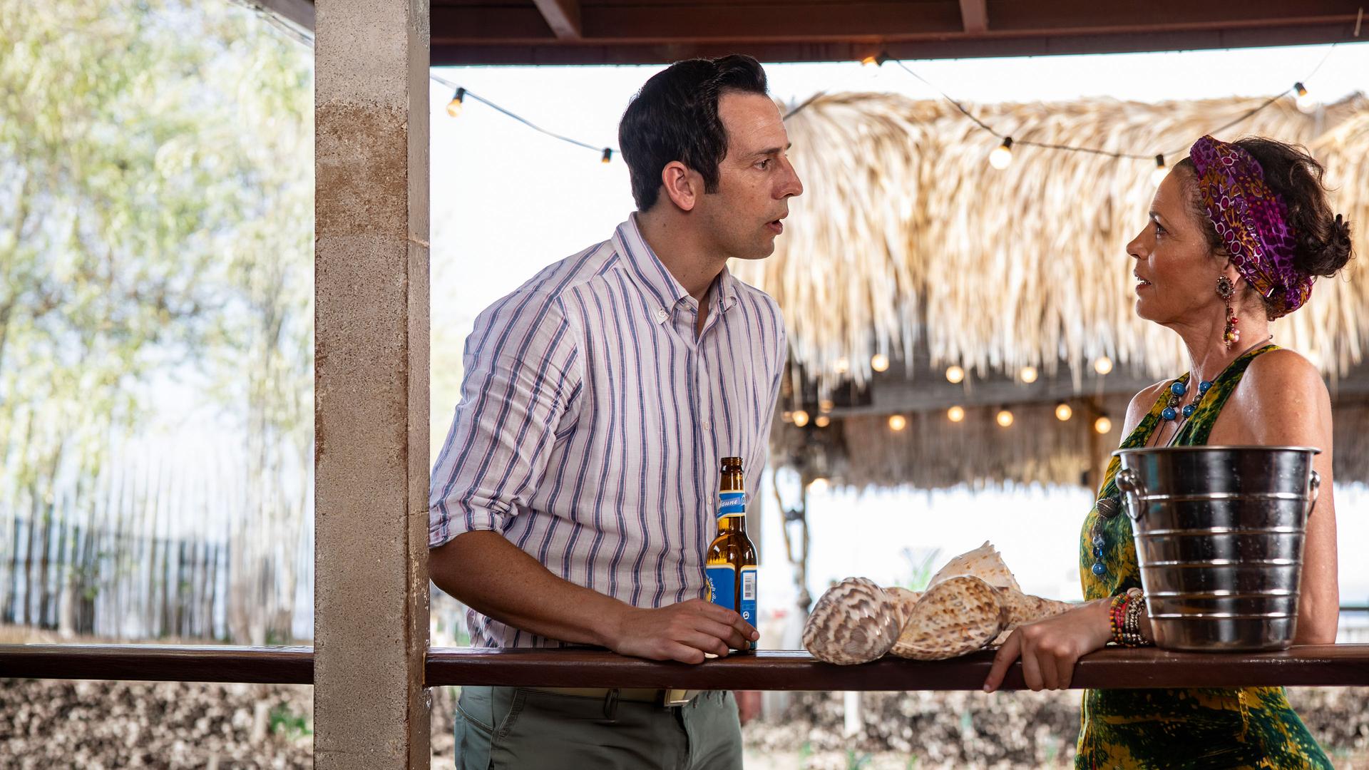 "Death in Paradise - Die Finsternis": Neville Parker (Ralf Little) und Catherine Bordey (Elizabeth Bourgine) stehen an einer Bartheke und reden miteinander.